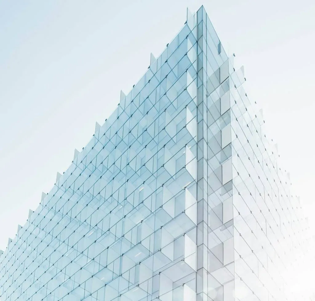 A modern glass building with a geometric design against a clear sky. The structure features repetitive square patterns, creating an optical illusion with light reflections. The lighting gives the building a translucent appearance.