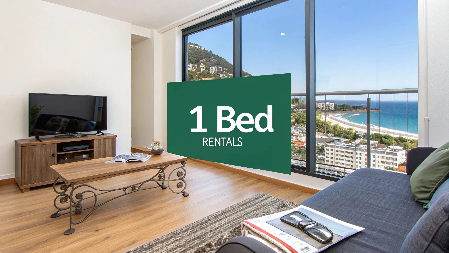 A modern living room with a wooden floor, TV, coffee table, and couch, featuring large windows overlooking the beach and ocean. A green sign reads 